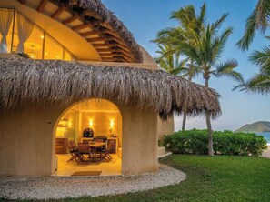 A thatched-roof structure with an interior dining area, palm trees, and a view of the sea. - Mar de Coco Areca 101 (Playa Blanca)