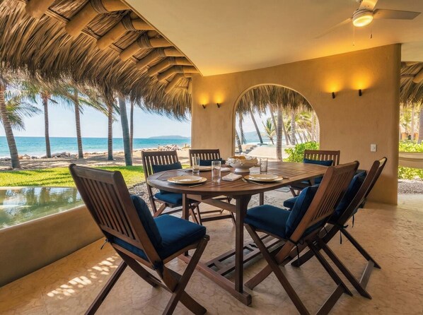 Mesa redonda con sillas para cuatro personas, en un cuarto con vista a la playa y palmeras.