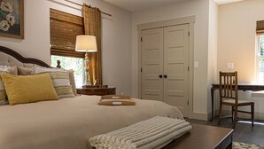 Un dormitorio ordenado con una cama grande, una mesita de noche con lámpara, una silla y un escritorio con asiento.