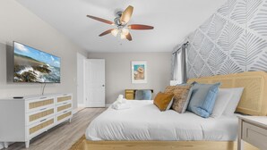 A bedroom with a bed, a ceiling fan, a TV, a dresser, and a door.