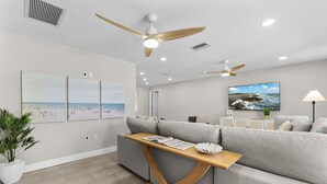 A modern living room with a grey sofa, wooden coffee table, ceiling fans, and wall-mounted artwork.