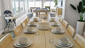 A dining area with a long table set for a meal, surrounded by chairs, with a pool table in the background.