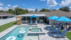A backyard with a swimming pool, lounge chairs, and umbrellas.