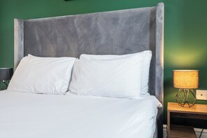 Restful retreat with a neatly made bed against a soothing green wall, complemented by a stylish nightstand and geometric lamp.