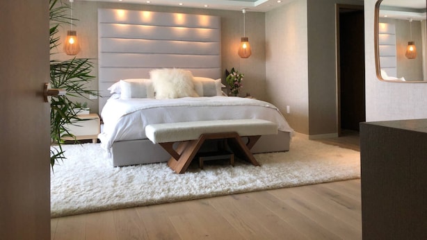 Ein modernes Schlafzimmer mit einem großen Bett, Nachttischen, einem flauschigen Teppich und einem Spiegel.
