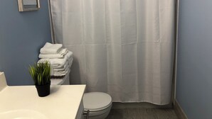 Ein Badezimmer mit Toilette, Waschbecken, einem Stapel Handtücher und einer Duschvorhang.
