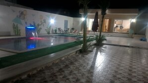 A nighttime pool area with a water feature and a mural on the wall.