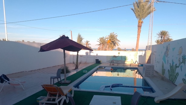 A swimming pool with lounge chairs and a table, surrounded by palm trees and a mural.