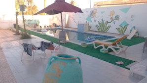 A pool area with lounge chairs, a large vase, and a mural on the wall.