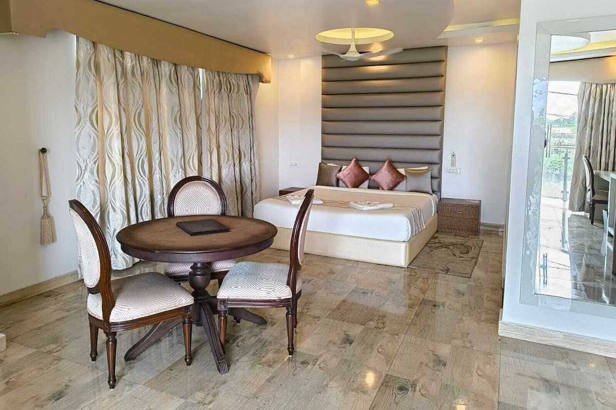 Une chambre d’hôtel avec une table et des chaises, un lit avec une tête de lit et une vue à travers une porte vitrée.