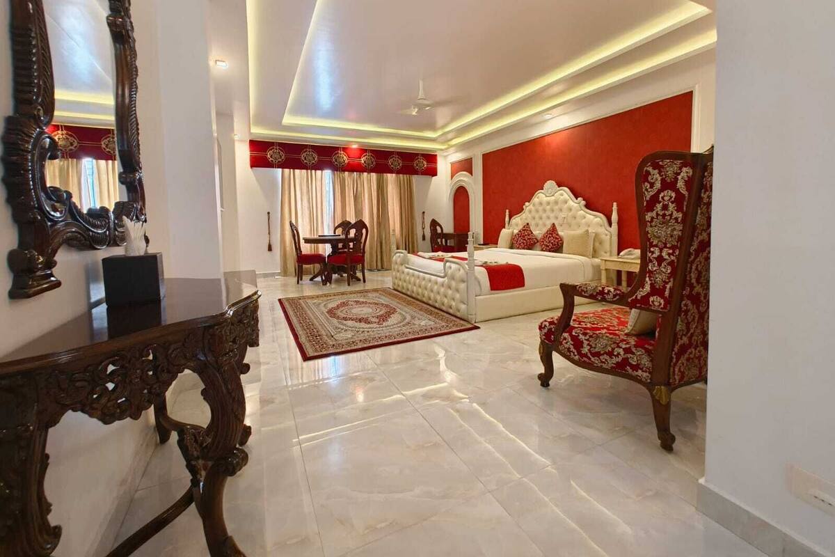 Une chambre avec un grand lit, un coin salon avec un fauteuil, une table à manger et un grand miroir.
