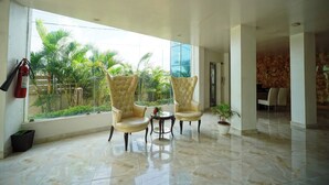 A spacious lobby with two plush armchairs, a small table, and a large window offering a view of palm trees.