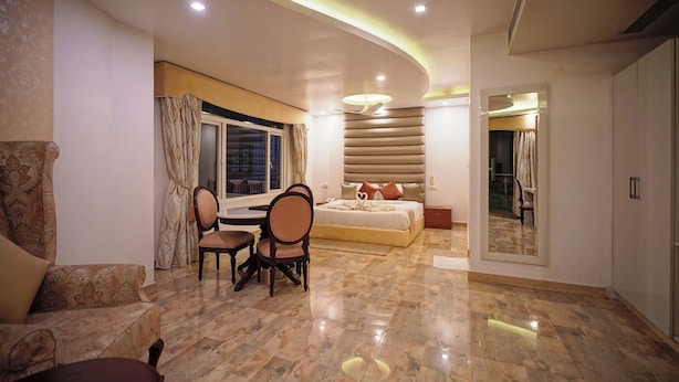 A modern hotel room with a dining area, a large bed, and a bathroom with a glass door.