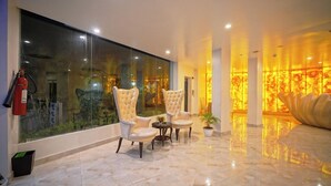 A modern lobby with marble flooring, two white tufted chairs, a small table, and a glass wall with a fire extinguisher.