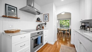 A modern kitchen with white cabinets, a stainless steel range hood, and a wooden dining table with chairs. - Mid-Century Modern Bungalow Near McKinley Park! (Sacramento)