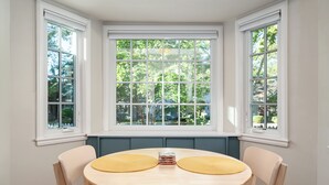 A dining area with a round table, two chairs, and a bay window with a view of trees. - Mid-Century Modern Bungalow Near McKinley Park! (Sacramento)