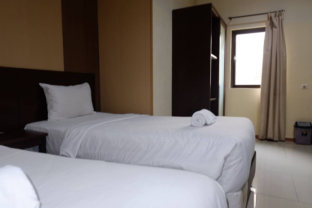A hotel room with two beds, a dark headboard, a wardrobe, and a window with curtains.