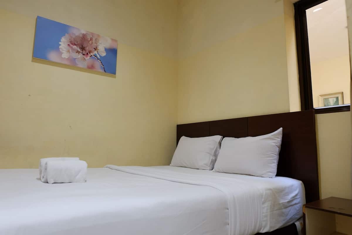 A neatly made bed with white linens and pillows, a framed floral artwork on the wall, and a small bedside table.