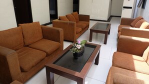 A hotel lobby with multiple brown sofas arranged around a central coffee table with a flower vase. - De Nusantara Hotel Syariah (Medan)