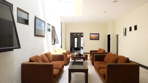 A spacious living room with two sofas and a coffee table, a flat-screen TV mounted on the wall, and a door leading to another room. - De Nusantara Hotel Syariah (Medan)