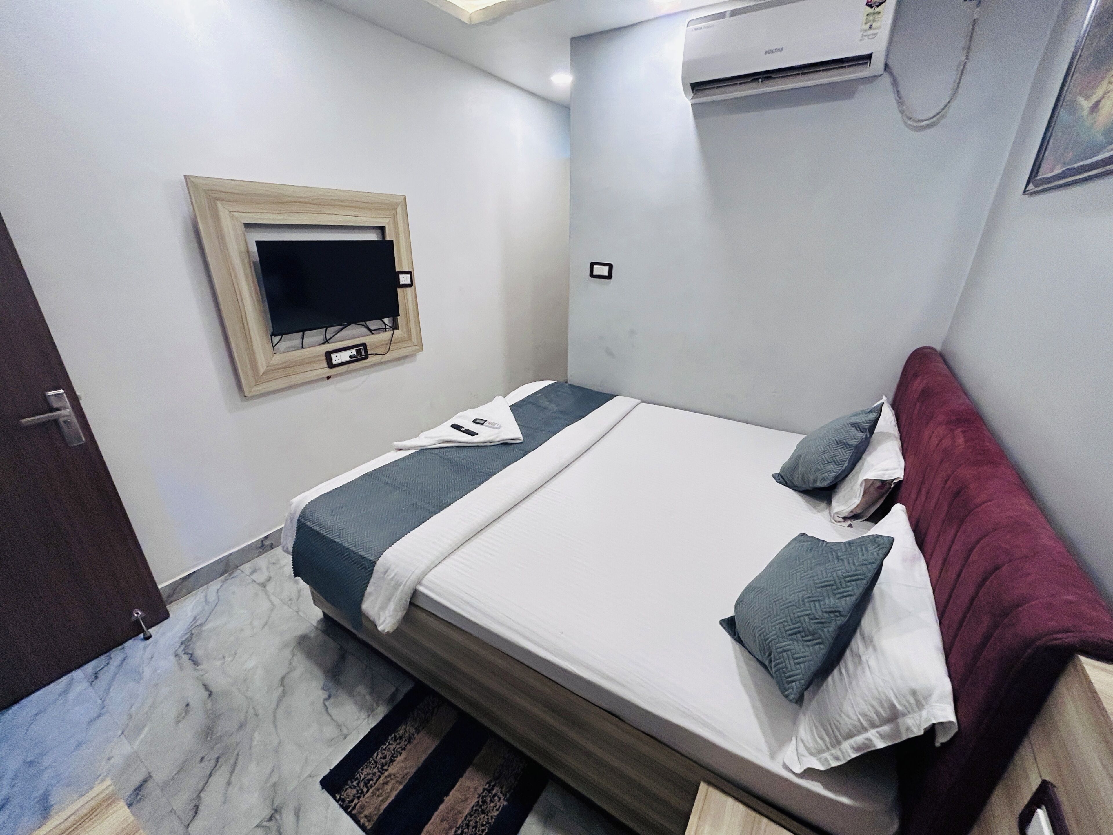 Ein Schlafzimmer mit Bett, einem an der Wand befestigten Fernseher, einer Klimaanlage und einer Tür.