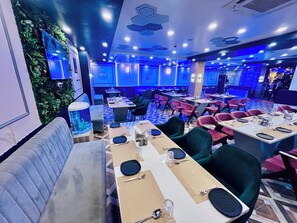 A restaurant with multiple tables, chairs, and a large aquarium. - Hotel Dwarka Palace (Darbhanga)