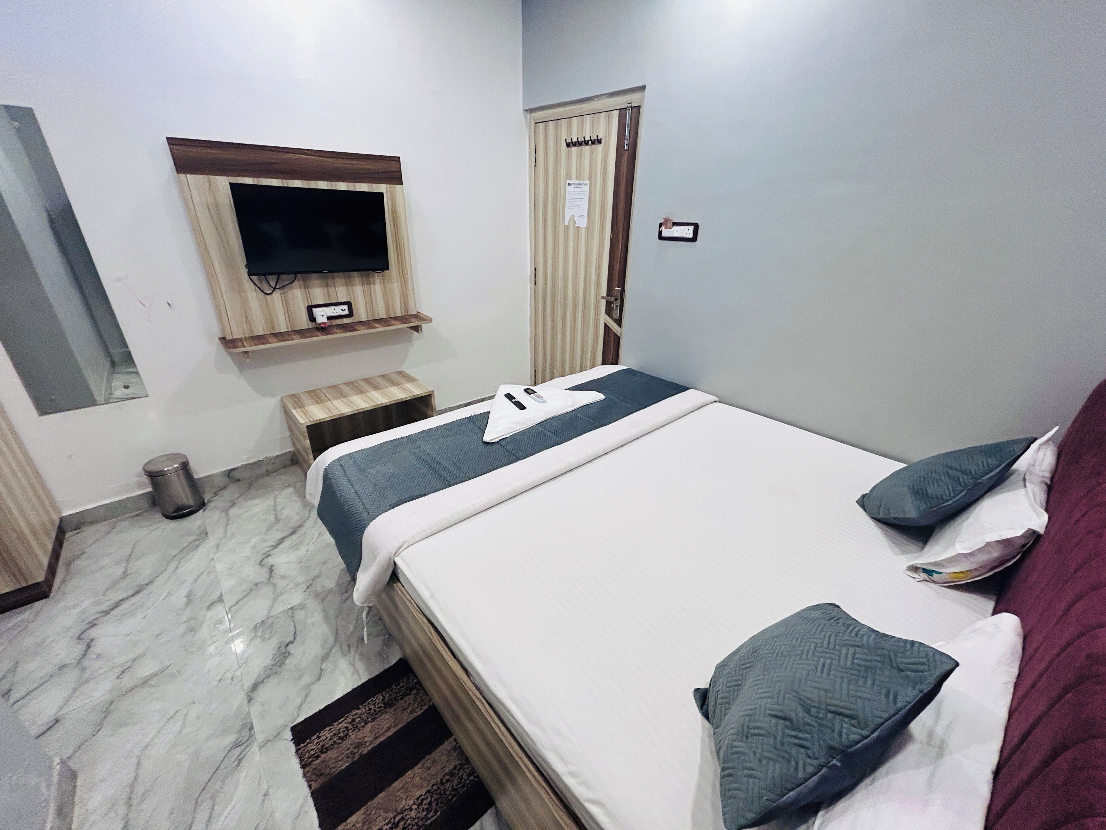 A hotel room with a bed, a television mounted on the wall, a small wooden stool, and a door with a sign.