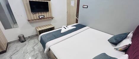 A hotel room with a bed, a television mounted on the wall, a small wooden stool, and a door with a sign.
