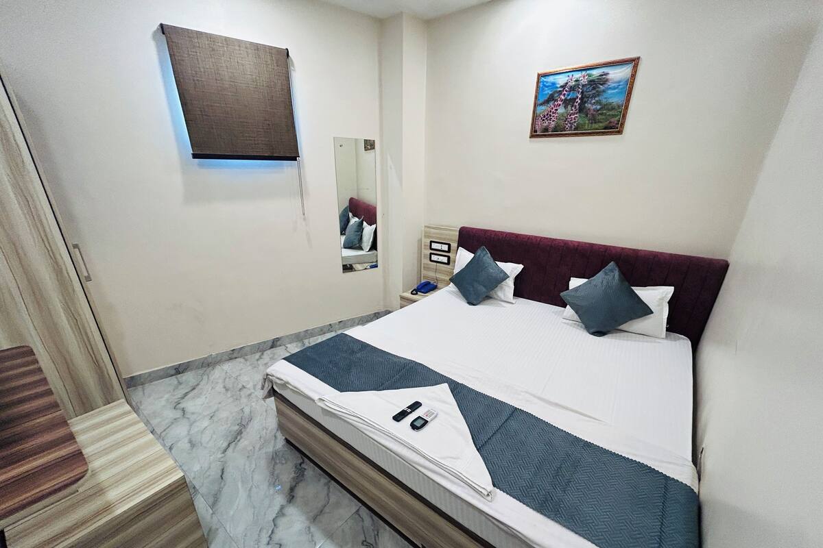 Una habitación de hotel con cama, mesita de noche, espejo, cuadro y puerta.