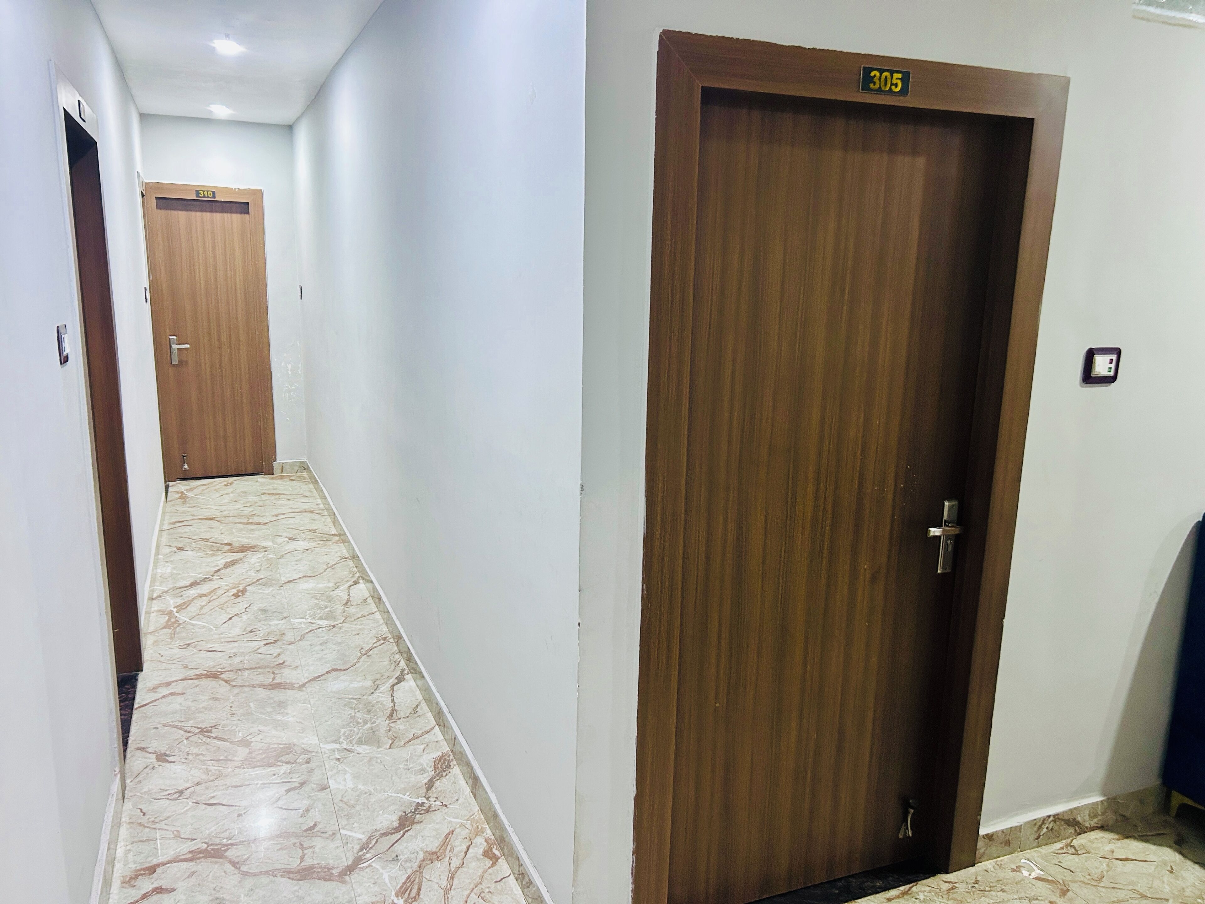 A hallway with marble flooring, wooden doors, and a ceiling light.