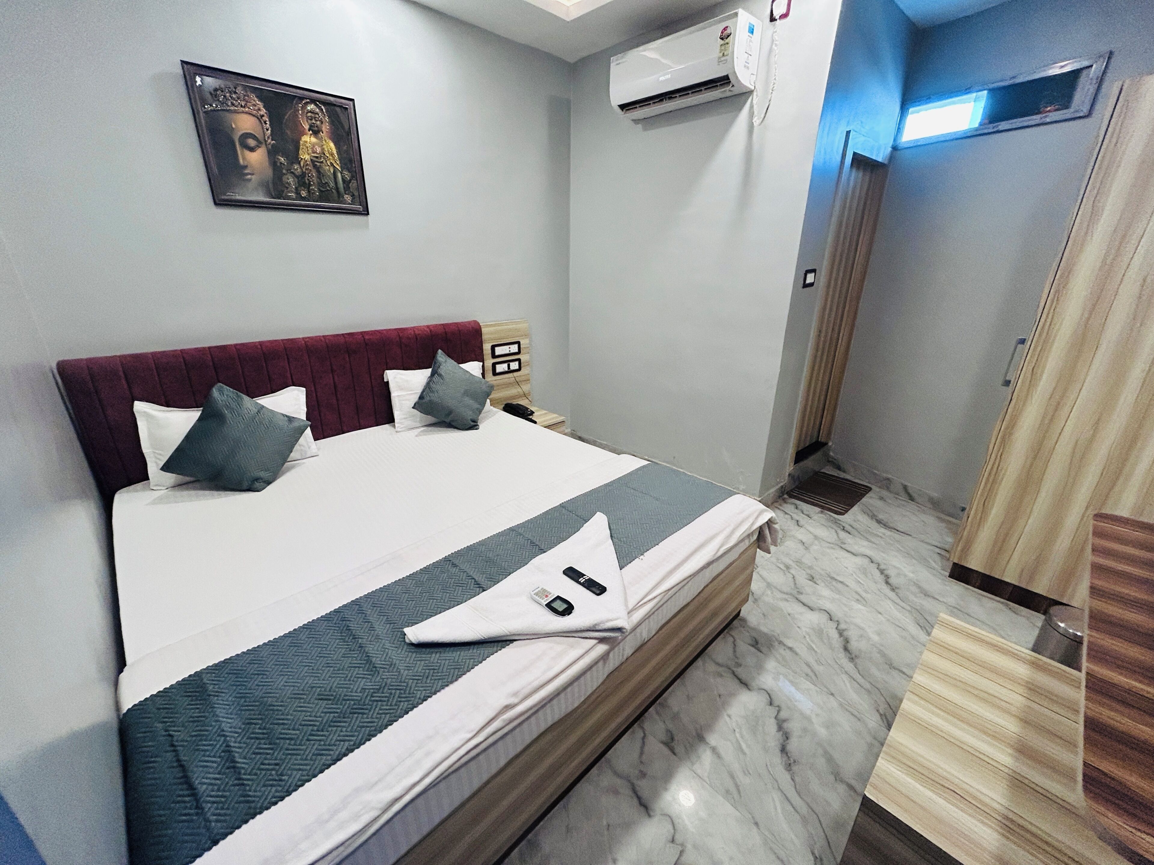 Une chambre d’hôtel avec un lit, un climatiseur fixé au mur, une porte et une petite fenêtre.
