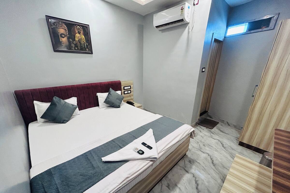 Habitación de hotel con cama, aire acondicionado en la pared, una puerta y un ventanal pequeño.