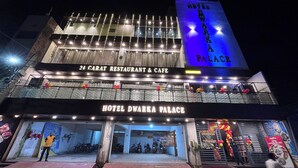 Ein Hotel mit einer auffälligen Schilder für 'Hotel Dwarka Palace' und '24 Carat Restaurant & Cafe' über dem Eingang.