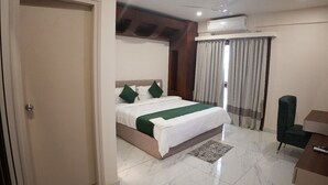 A hotel room with a bed, a desk, a chair, a ceiling fan, and an air conditioning unit. - AK CASTLE SUITES (Bengaluru)