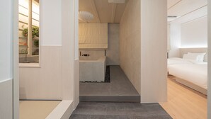 Habitación de hotel moderna con diseño minimalista, que incluye una cama, un pequeño rincón de descanso y vistas al exterior.