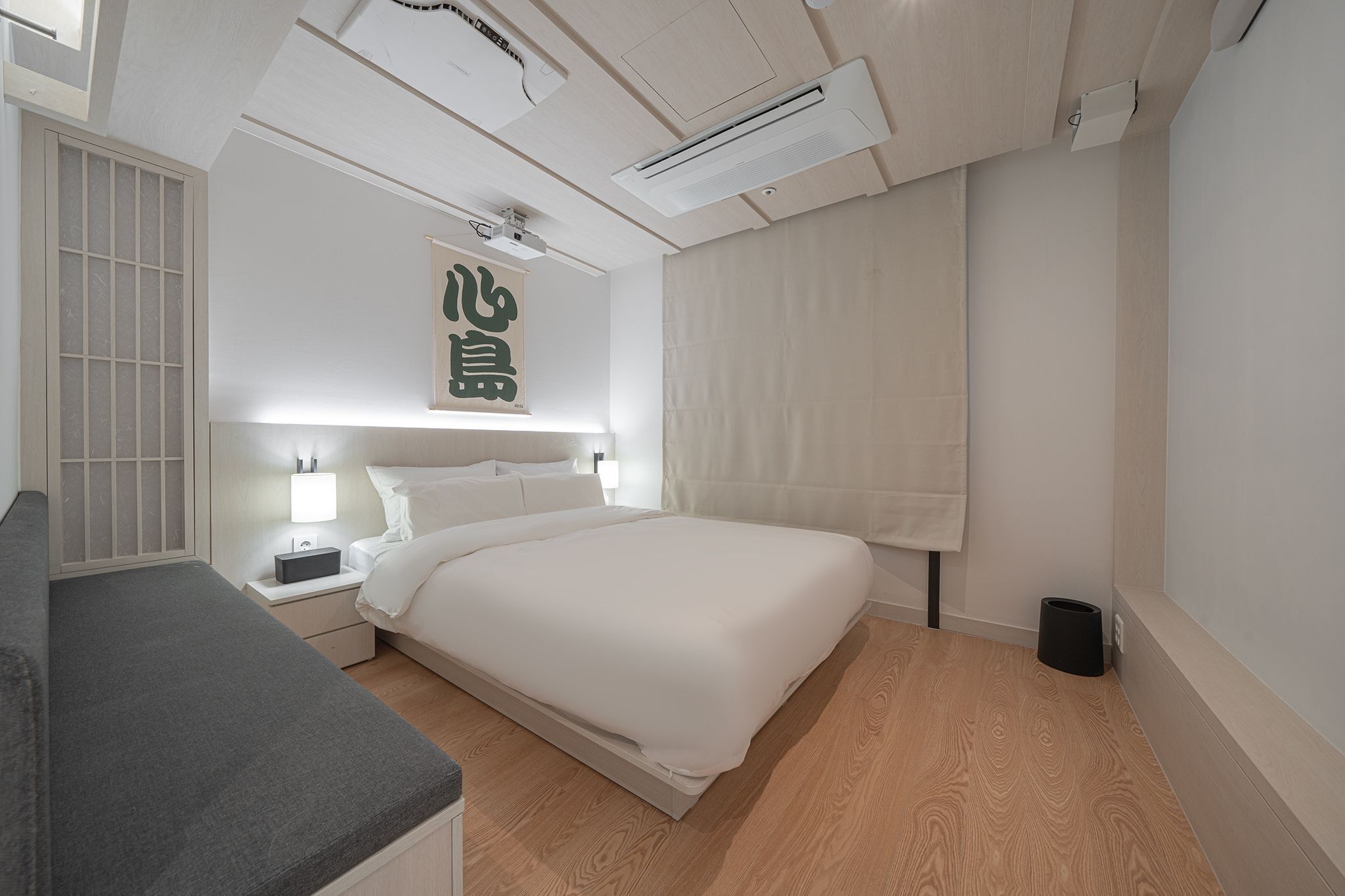 Ein modernes Schlafzimmer mit einem ordentlich bezogenen Bett, Nachttischen inklusive Lampen und einem großen Fenster mit Vorhängen.