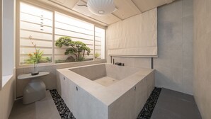 Un baño moderno con una bañera grande, un lavamanos pequeño y una ventana con vista a la vegetación.
