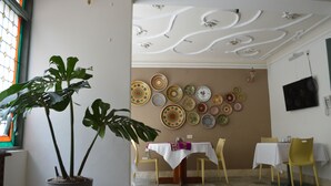 Zona pranzo con tavolo apparecchiato per due, una pianta in vaso e parete decorata con piatti.