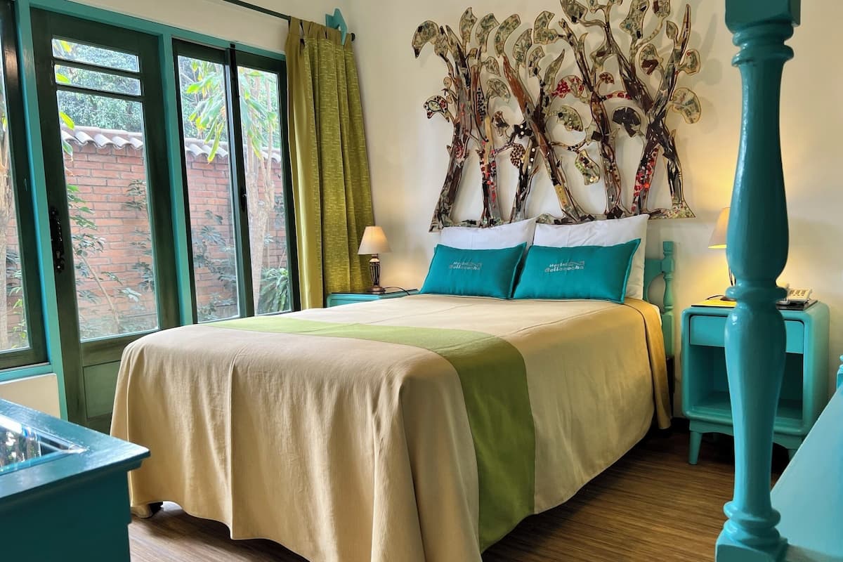 A hotel room with a bed, a nightstand, a lamp, and a decorative tree wall art.