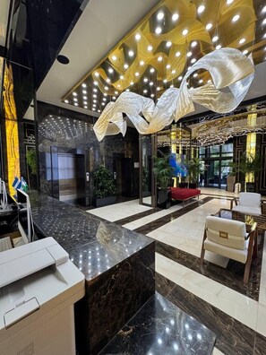 A modern lobby with a marble floor, a reception desk, a red sofa, and a large abstract light fixture. - Azimut Hotel Tashkent (Tashkent)