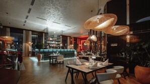 Un ristorante moderno con pavimento in legno, tavoli con sedie bianche e lampadari in vimini.