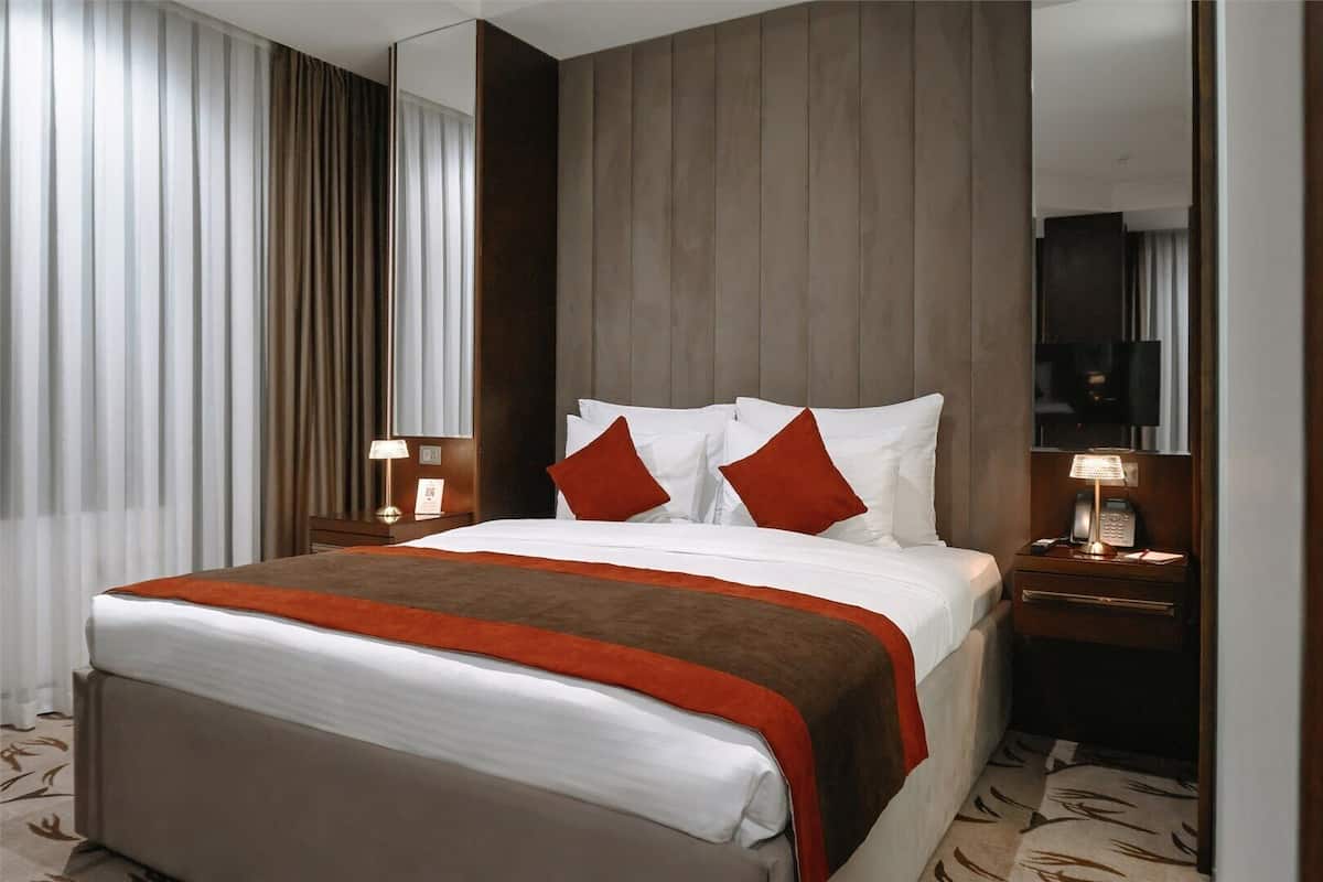 Une chambre d’hôtel avec un grand lit, deux tables de chevet, un miroir et une fenêtre avec des rideaux.