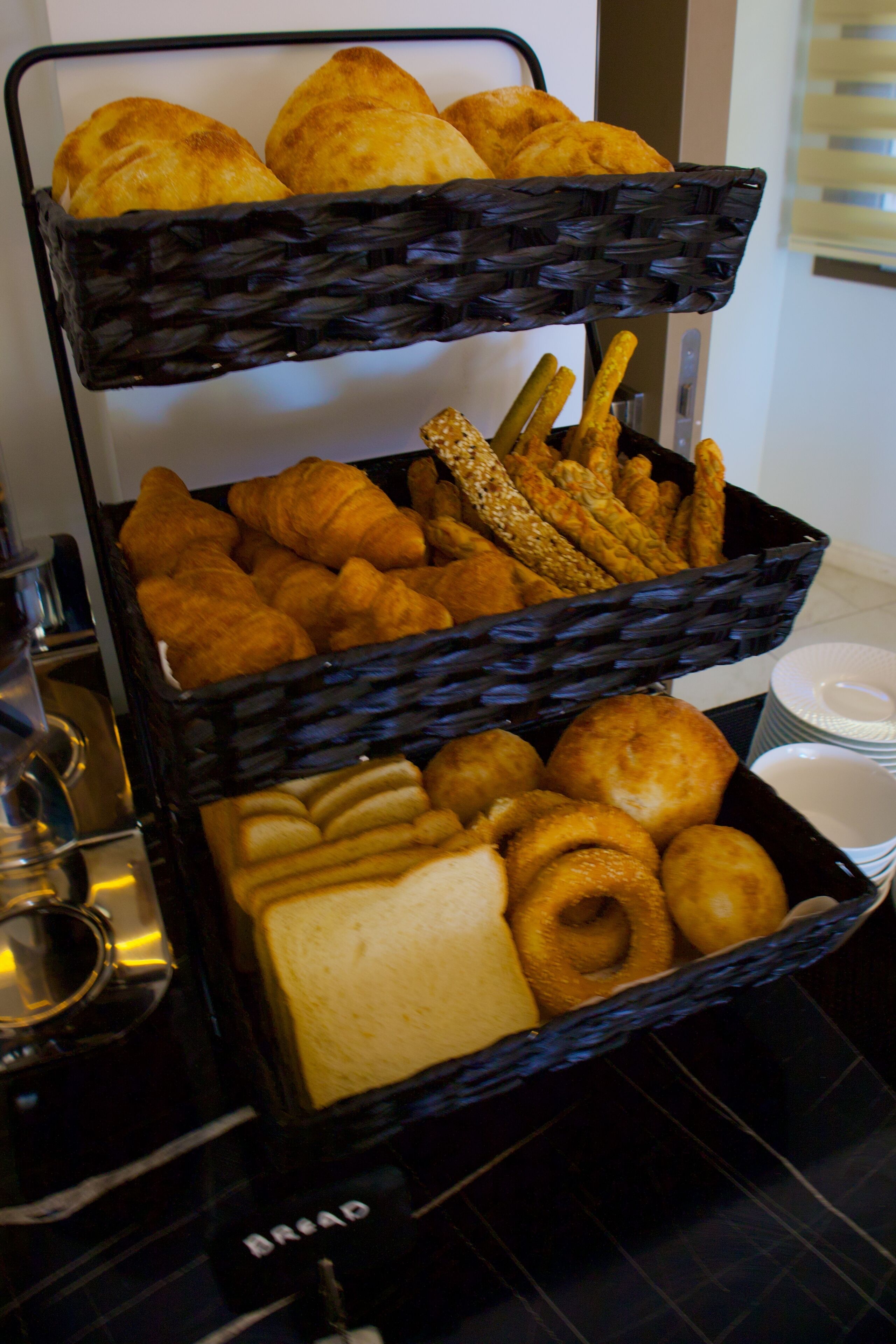 A three-tiered basket filled with various baked goods including croissants, bread rolls, and pastries.