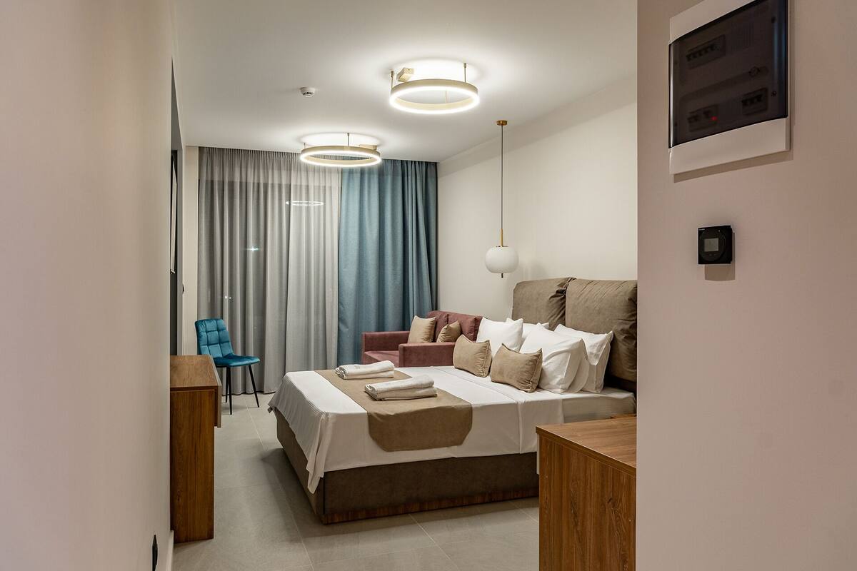 Una habitación de hotel moderna con una cama grande, un escritorio y una silla. Hay cortinas y una lámpara en el techo.