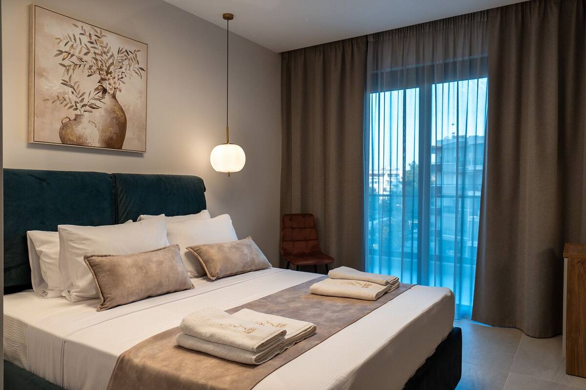 Habitación de hotel con una cama grande, vistas de la ciudad a través de la ventana, un cuadro en la pared y una lámpara colgante.