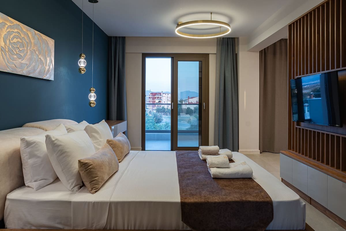 Habitación de hotel moderna con una cama grande, televisión y balcón con vista a la ciudad.