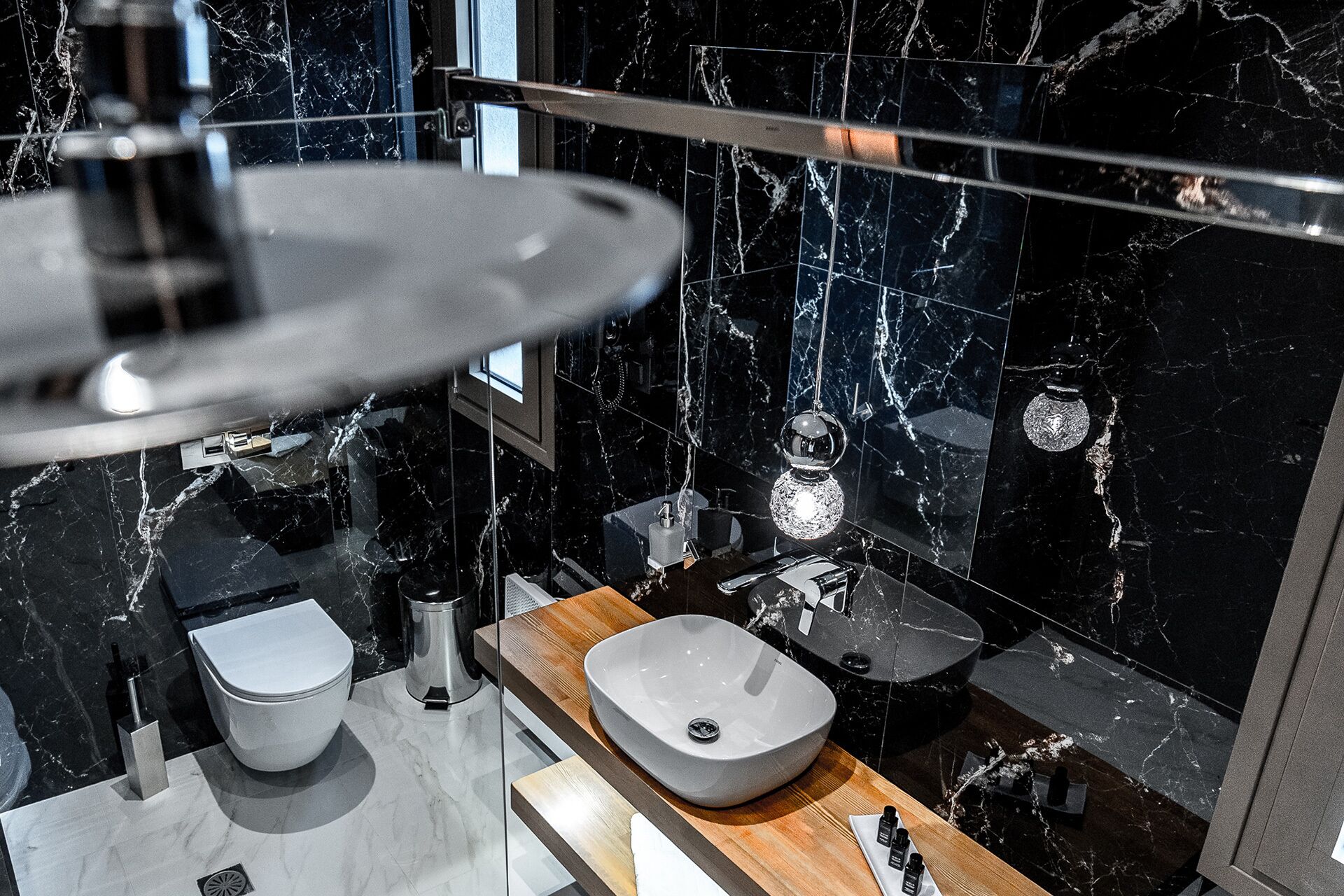 A modern bathroom with a marble backsplash, a wooden vanity, a vessel sink, and a toilet.