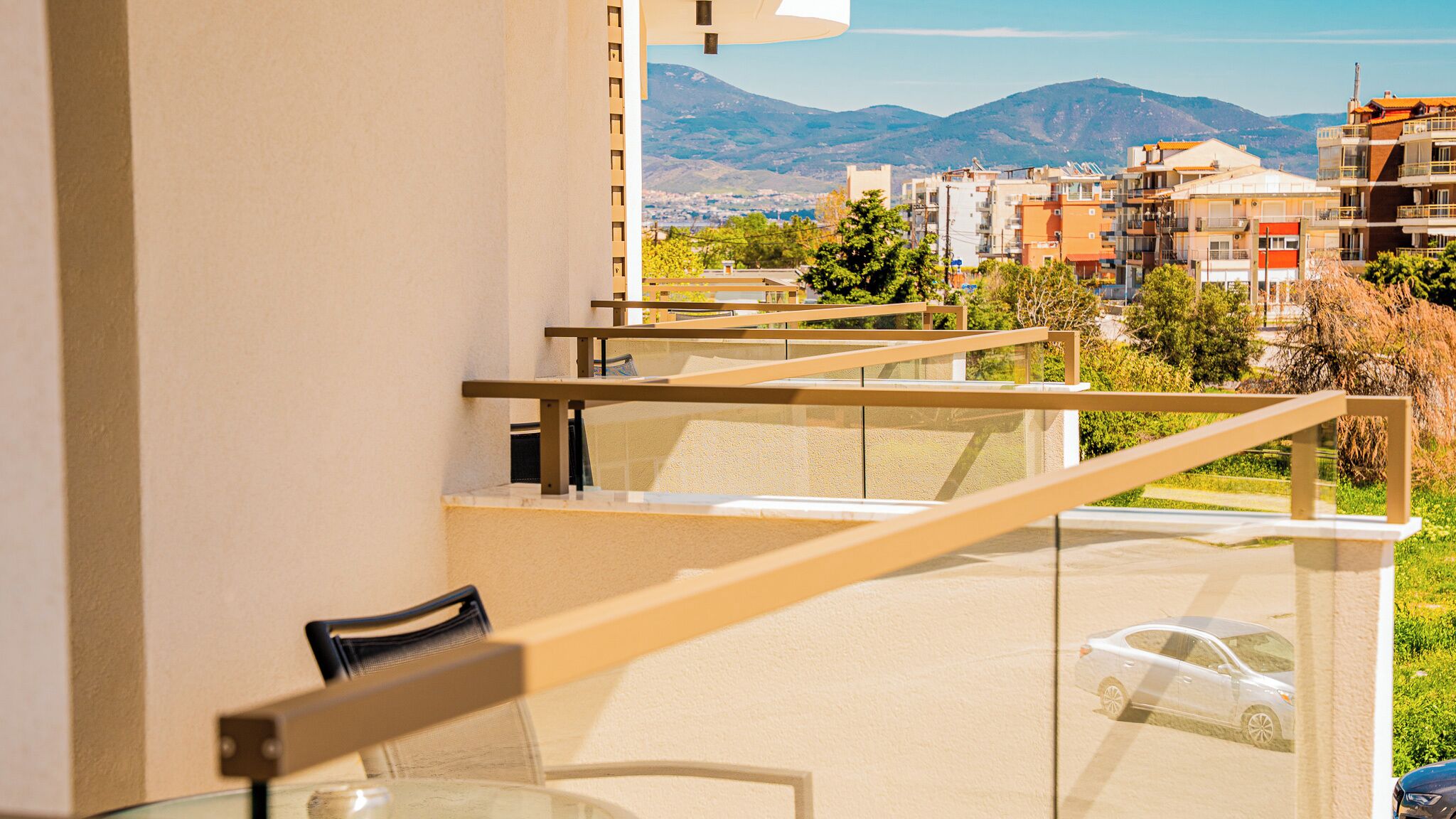 A balcony with a glass railing overlooking a cityscape with buildings and mountains in the distance.