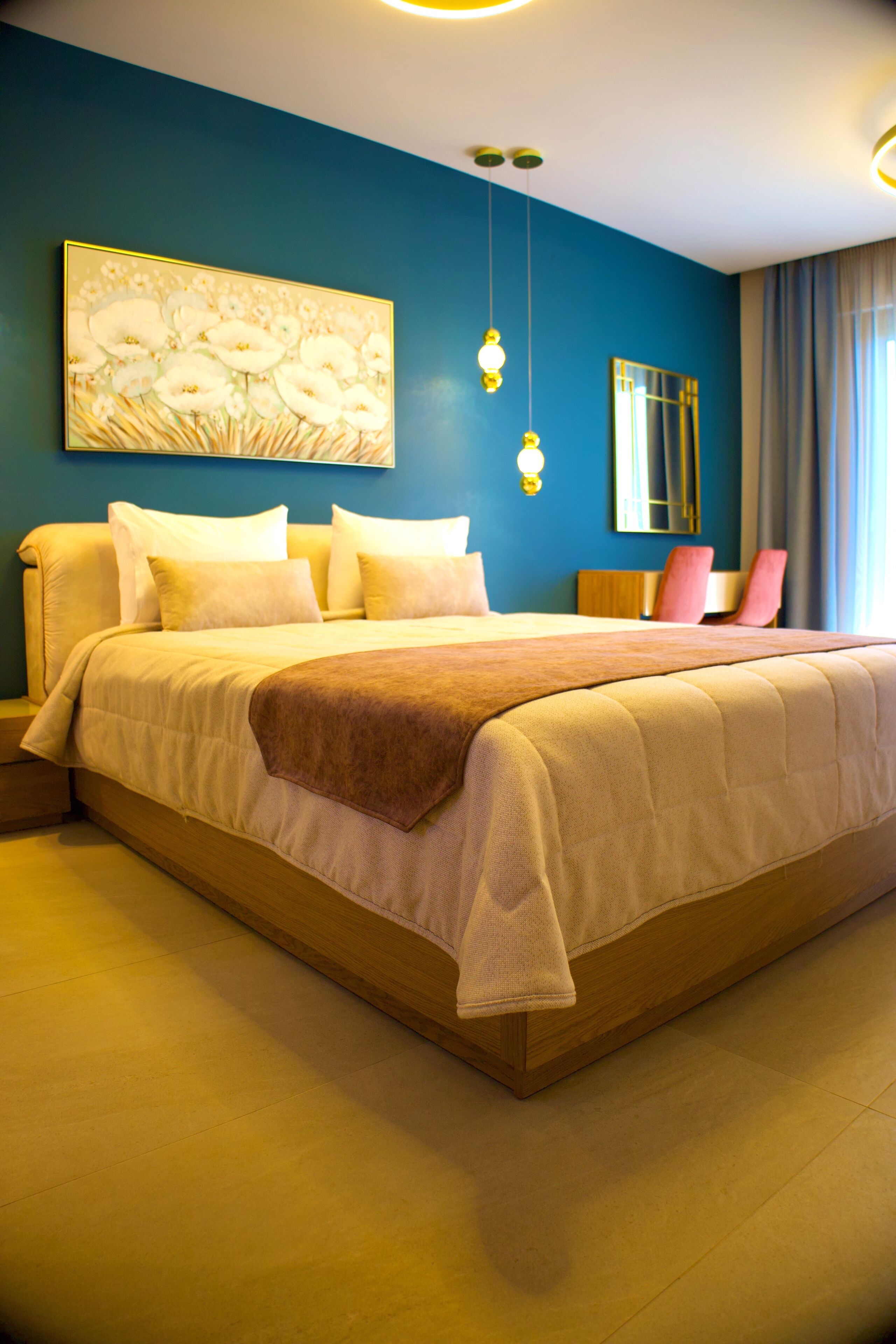 Een groot bed met een beige en bruine spreideken, een houten hoofdbord en een aan de muur bevestigd schilderij van witte bloemen.