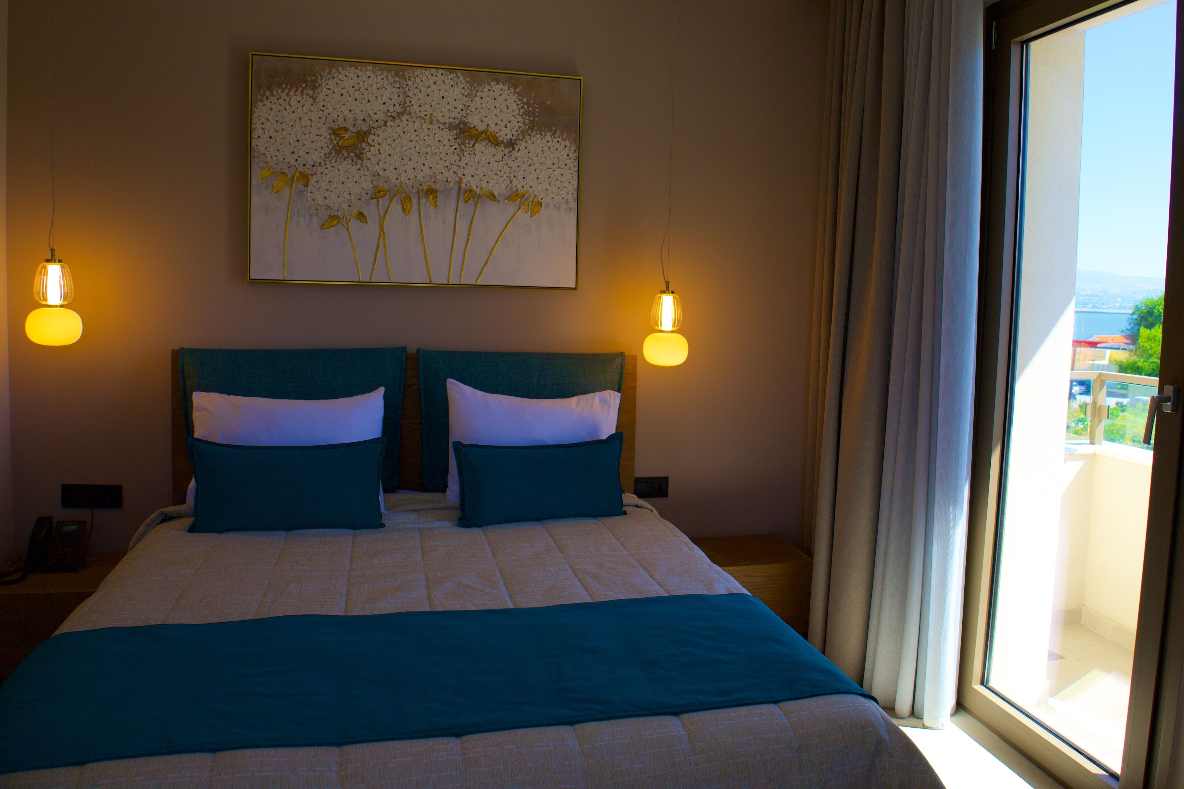A hotel room with a large bed, two bedside tables, a nightstand, a painting on the wall, and a window with curtains.